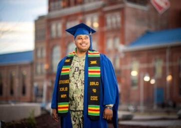 Jameer Fitch wearing his cap and gown over his military uniform standing in front of the Tivoli